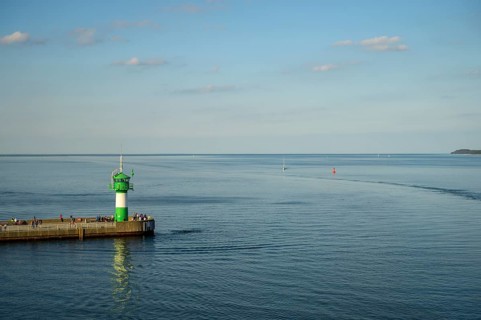 A green lighthouse harbour fire stands on a pier at the port exit of Travemünde in front of a calm,