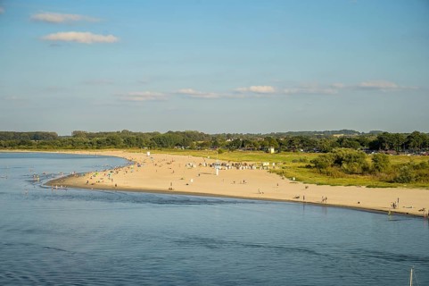 A sunny beach on Priwall near Rosenhagen with people on the shore, surrounded by green countryside
