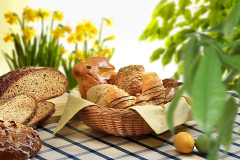 Easter basket with pastries, bread, Easter eggs, on checkered tablecloth, plants and flowers as