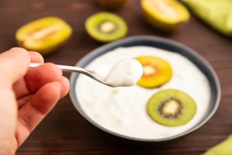 Yogurt, with kiwi in blue bowl on brown wooden background and green linen textile with hand, side