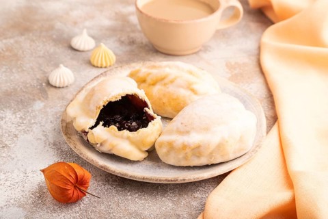 Glazed Pies with blueberry jam on brown concrete background and orange linen textile, cup of