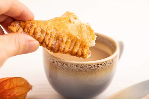 Triangles Pie, Puff Pastry, Samsa with cherry jam with hand on white wooden background, cup of