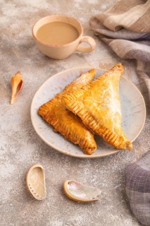 Triangles Pie, Puff Pastry, Samsa with cherry jam on brown concrete background and linen textile,