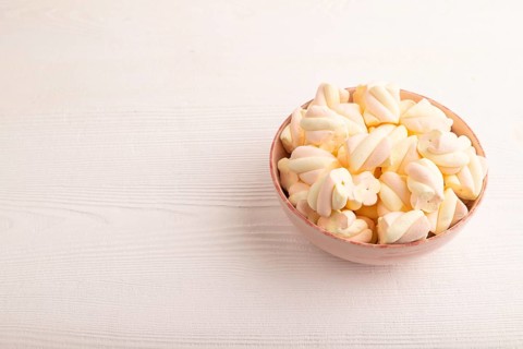 Orange and pink marshmallow in ceramic bowl on white wooden background, side view, copy space,