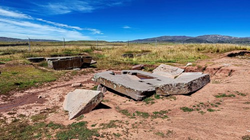 Broken stone structures are spread across the vast countryside, under a clear sky, the
