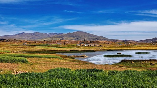 Wide landscape with a lake surrounded by meadows and small villages under a blue sky, The landscape