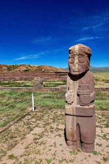 Free-standing stone statue in a grass-covered ruined landscape under a blue sky, The archaeological