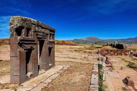 Ancient stone structures in a vast, mountainous landscape under clear blue skies, the