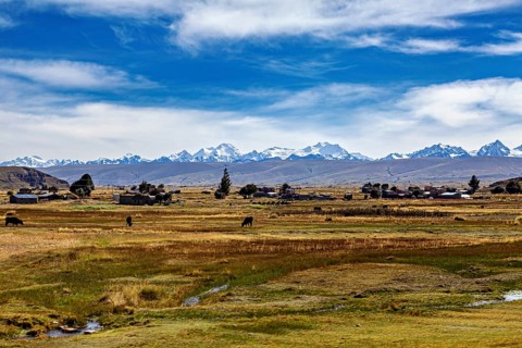 Landscape with snow-capped mountains in the background, village and fields in the foreground under