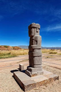 Ancient stone figure standing upright on a platform against a clear sky, the archaeological site