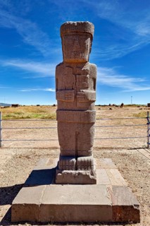 Ancient stone statue on a base in an open-air area under clear skies, The archaeological site with
