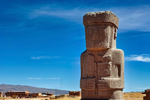 Large ancient stone statue under clear sky, showing detailed engravings, the archaeological site