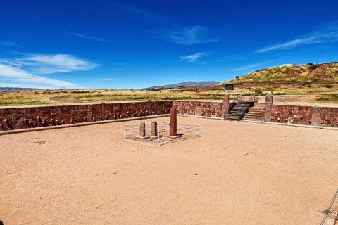 A rectangular square with stone pillars surrounded by ruins under a clear sky, The archaeological