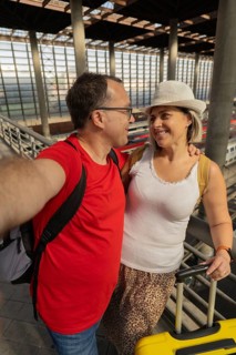Smiling adult travel couple taking a selfie while looking at each other inside a modern train