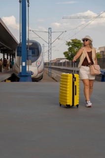 Middle aged woman pulling a bright yellow suitcase on a modern urban train platform, enjoying a