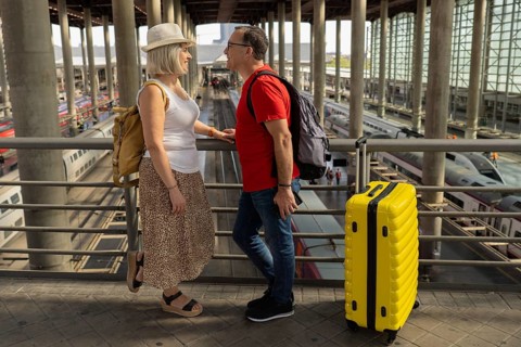 Happy mature tourist couple standing inside a large railway station, enjoying their journey with