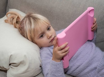 Portrait of a blonde girl, 4 years old, lying down reading a tablet in Ystad, Skåne County, Sweden,