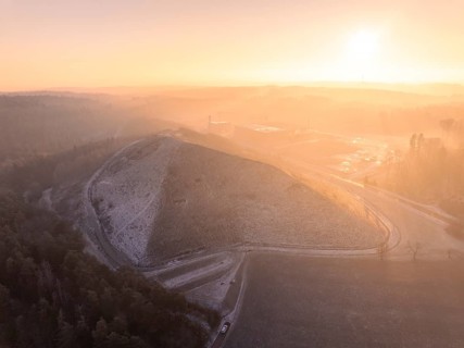 Landscaped hills in the pink-yellow light of sunrise, old deposit, construction site for PV open