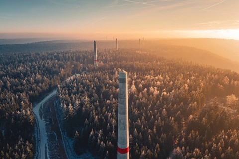 Narrow wind turbine towers rise above a snow-covered forest, winter silence and a curved path, in