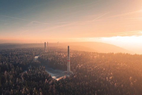 Dawn over a foggy forest with several wind turbine towers rising from the trees, Windkraft Bau,