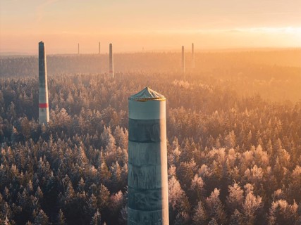Wind turbine towers stand in orange light in the morning over a forest surrounded by thick fog, a