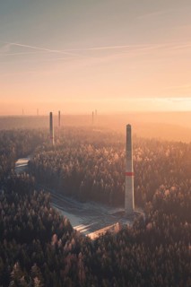 Wind turbine towers tower above a forest at sunset, soft pastel colors and fog create a quiet