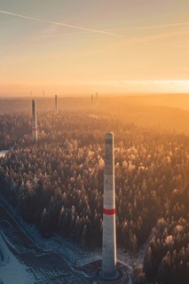 Wind turbine towers over a forest criss-crossed with snow trails, in warm sunlight, create a