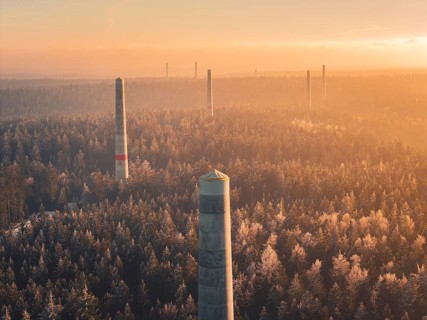Wind turbine towers rise above a sea of forest, soft shades of fog characterize the twilight hour,