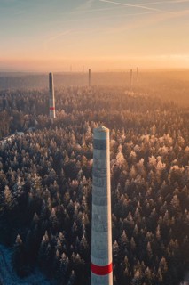 High wind turbine towers over frozen forest at sunrise, clouds of fog over the landscape, Windkraft