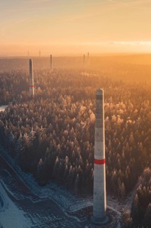 Wind turbine towers over snow-covered trees, the warm light and the fog create a mystical scene