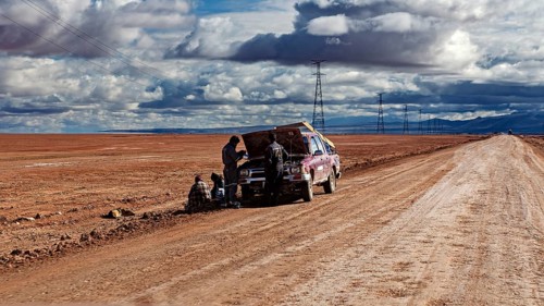 A car is being repaired on the side of the road by several people in the desert, The landscape of