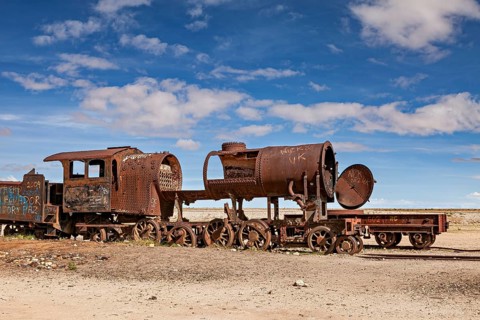 A heavily weathered locomotive with missing parts against a blue sky, old rusty locomotives at the