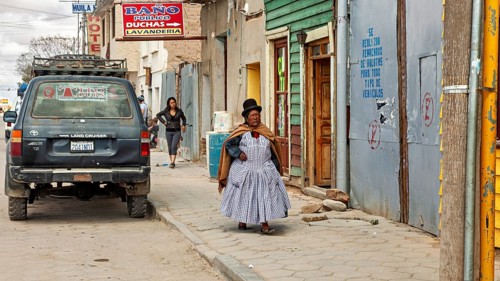 Woman wearing traditional clothes wearing melon walks on a sidewalk with colorful houses and
