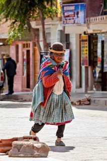 Elderly woman in traditional clothes with melon and colorful scarf walks on cobblestone street,