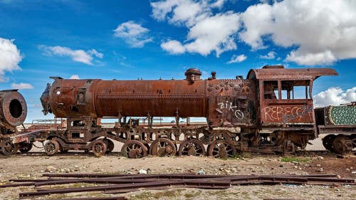 Rusted locomotive under a cloudy blue sky with graffiti along the body, old rusty locomotives at