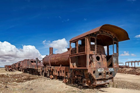Rusted locomotive in the desert under a clear blue sky with scattered clouds, old rusty locomotives