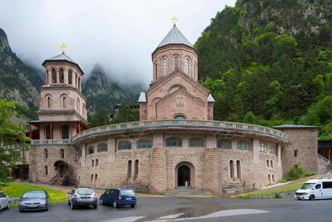 Historic monastery building surrounded by mountains and clouds in a peaceful atmosphere, Dariali