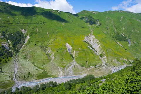 Green mountains and valleys with flowing river under blue sky, viewpoint near Gudauri, view of the