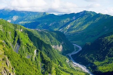 Green alpine landscape with a meandering river and majestic mountains in the background, landscape