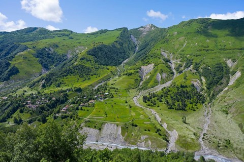 Green valley with mountains and river under blue sky and few clouds, viewpoint near Gudauri, view