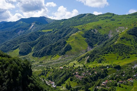 Lush green mountains with scattered village under blue sky and clouds, viewpoint near Gudauri, view