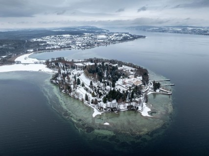 The wintry and snowy Mainau island in Lake Constance with the pier and the baroque Mainau Castle,