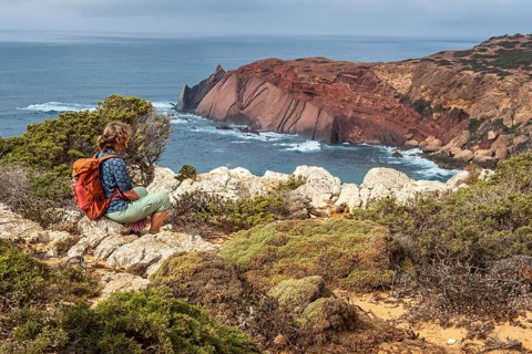 Hiking woman takes a break, view over cliff, Fishermens Trail, Rosa Vicentina, western Algarve just