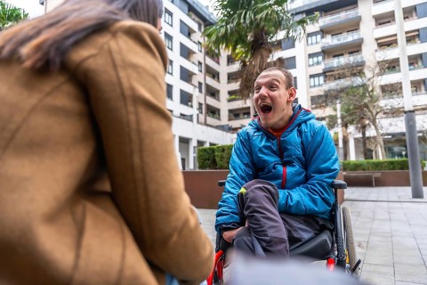 Disabled young man sitting in a wheelchair expressing joy and communicating with a caregiver or