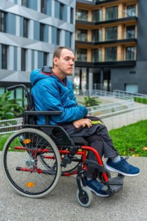 Young man living with a disability sitting in a manual wheelchair on a paved path outside modern