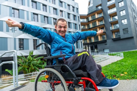 Smiling man in a wheelchair with arms outstretched expressing joy and freedom while navigating an