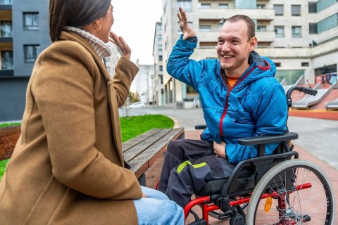 Joyful disabled man in a red wheelchair sharing a high five with a woman on a bench, symbolizing
