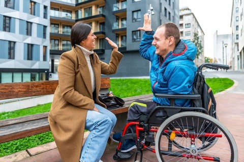 Young man with a physical disability sitting in a wheelchair and celebrating with a high five,