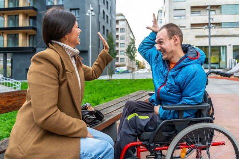 Young woman on a bench in the city happily high fiving a smiling man in a wheelchair, illustrating