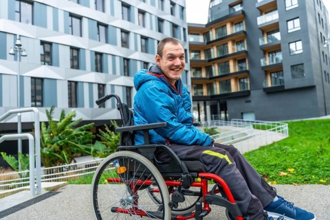 Happy man with a disability using a wheelchair on an accessible ramp in front of modern buildings,